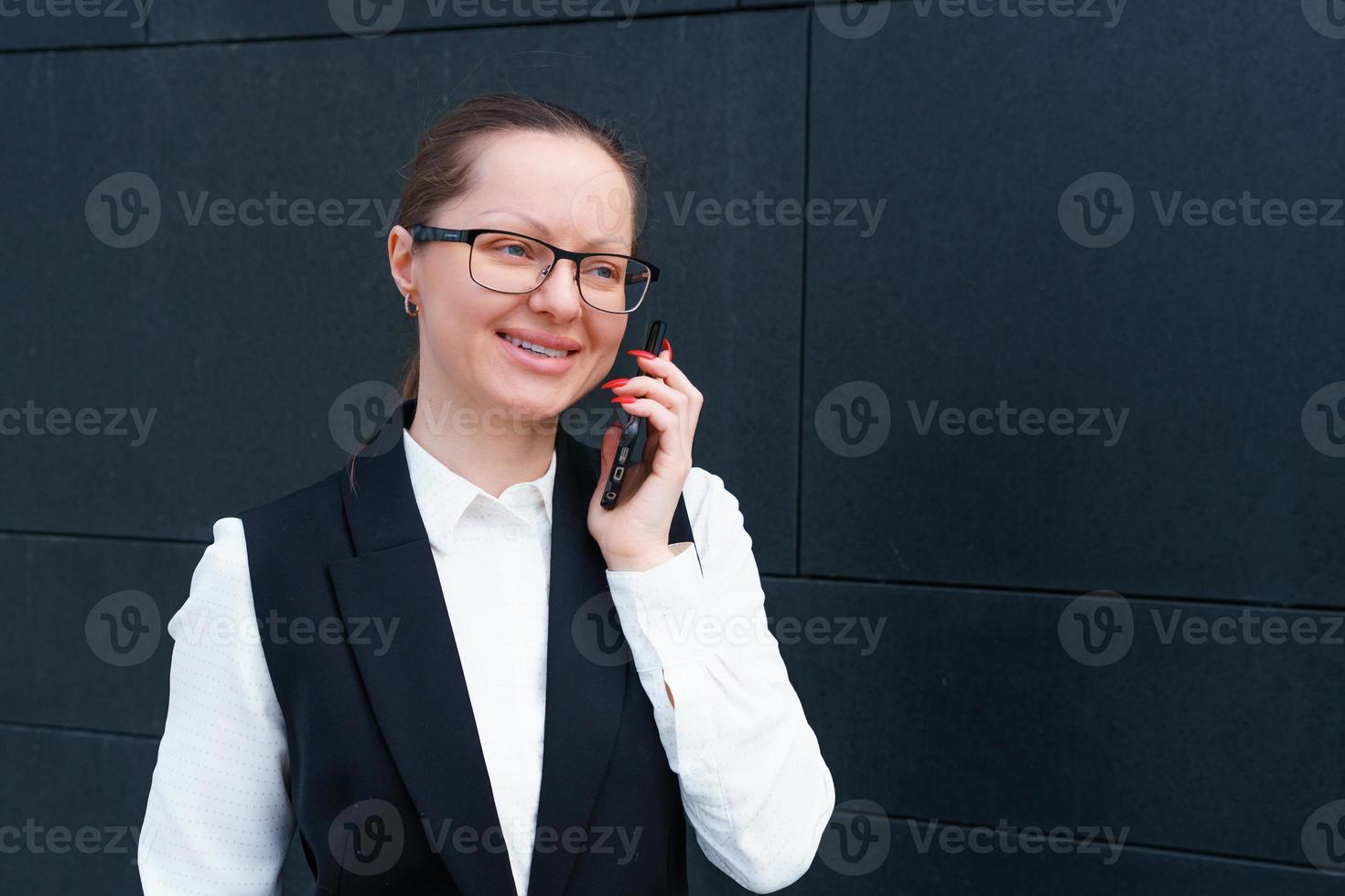 Successful businesswoman talking on mobile phone while walking outdoors near photo