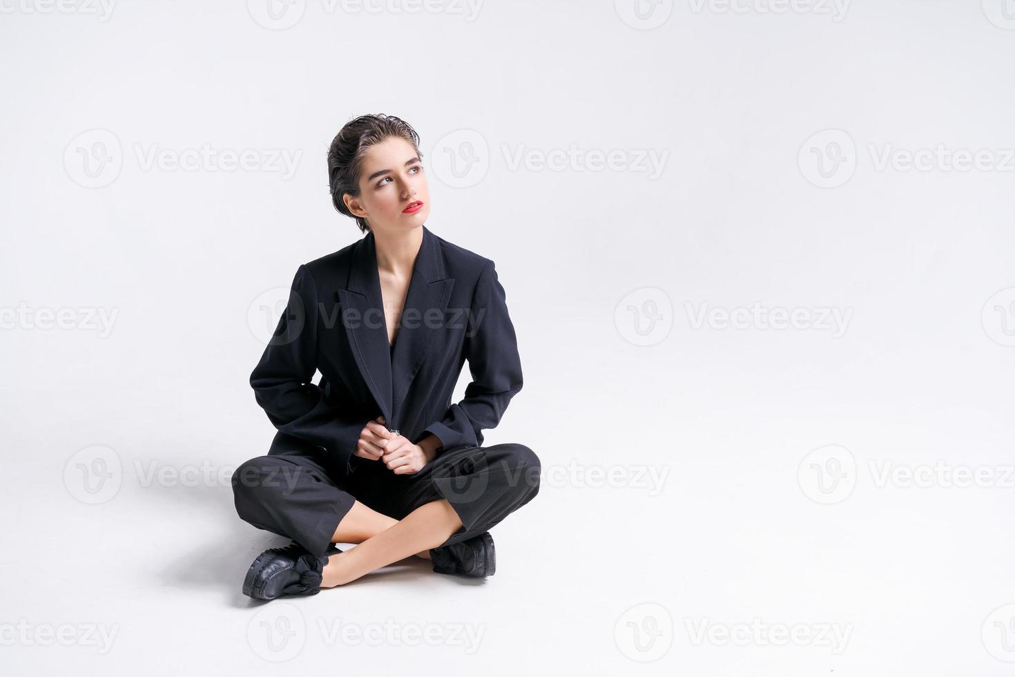 Beautiful young businesswoman in trendy black suit posing sitting on floor photo