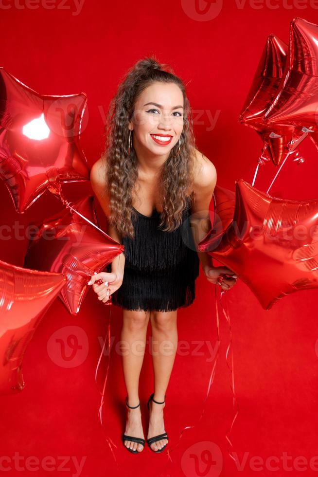 Beautiful young joyful girl is holding bunch red star balloons on red photo