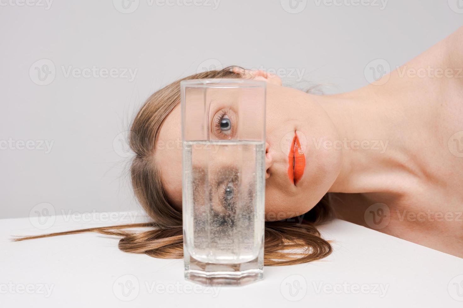 Beautiful woman looking through glass water looks into camera, bright orange photo