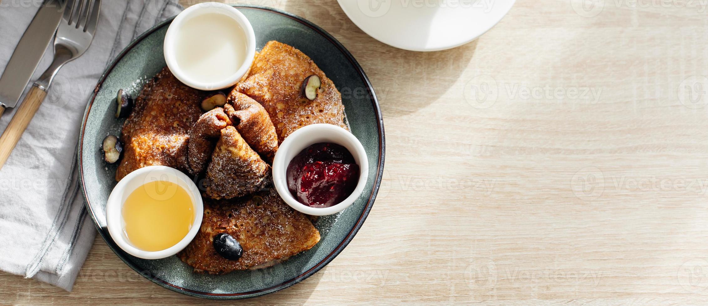 Delicious thin pancakes with jam, honey and sour cream and cup of tea on light wooden table. Morning breakfast concept. Top view with space for text. photo