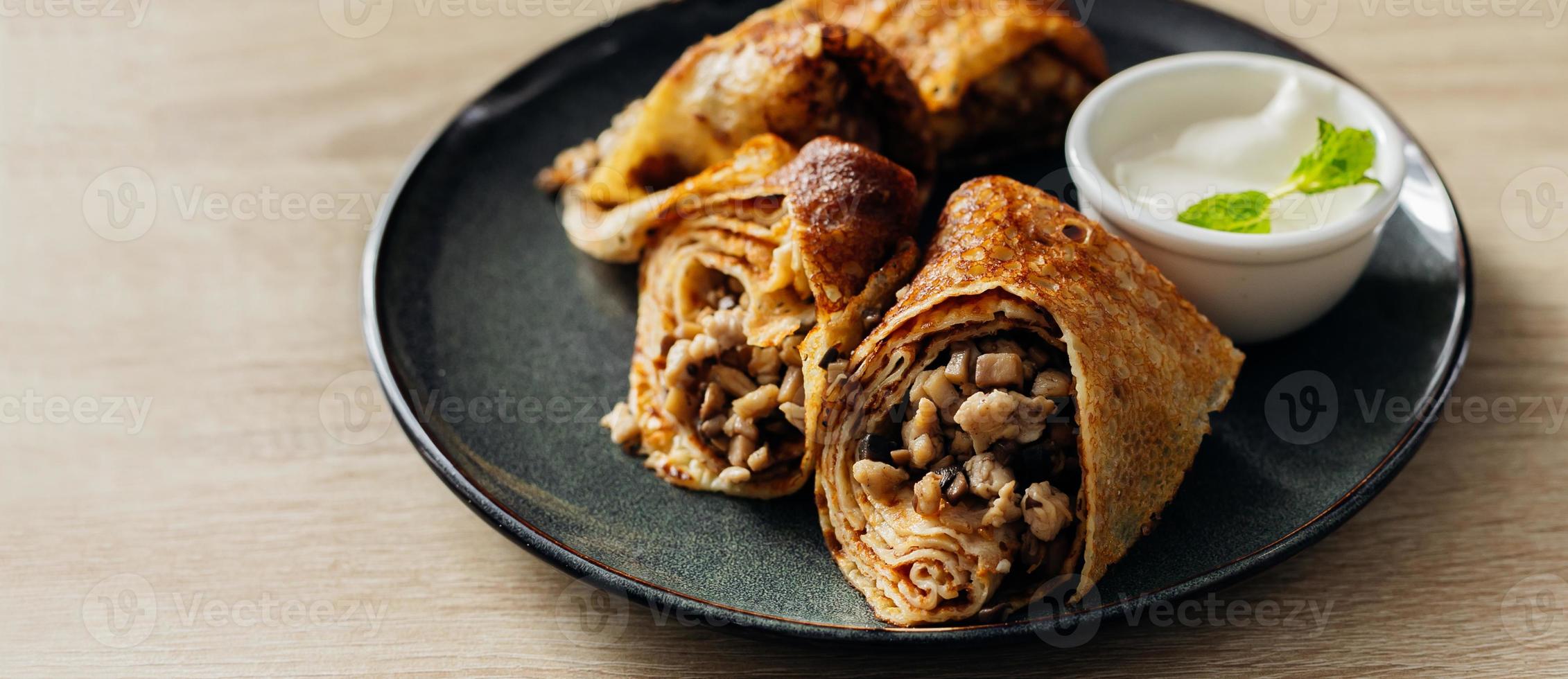 Crepes stuffed with chicken and mushrooms with sour cream on the wooden table. Banner for website. photo