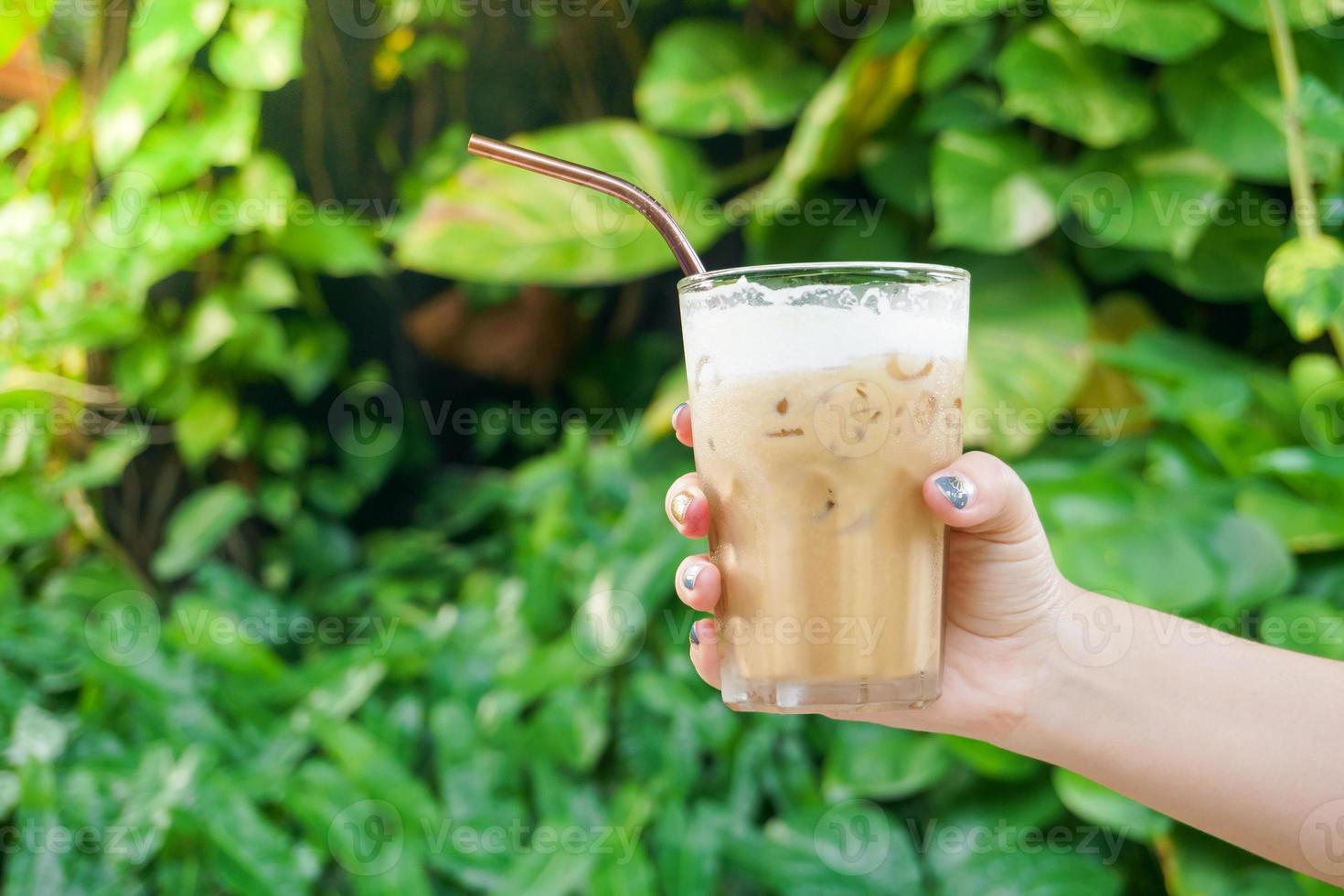 mujer de la mano sosteniendo el café helado de vidrio sobre fondo verde de la naturaleza, café con leche helado foto