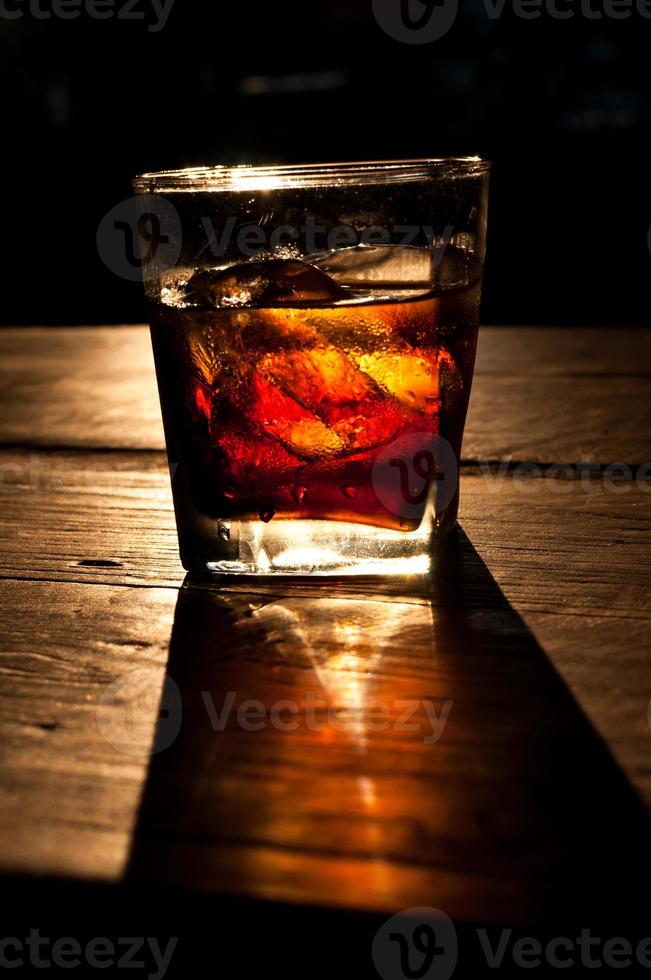 Cola with whiskey and ice on a wooden table background photo