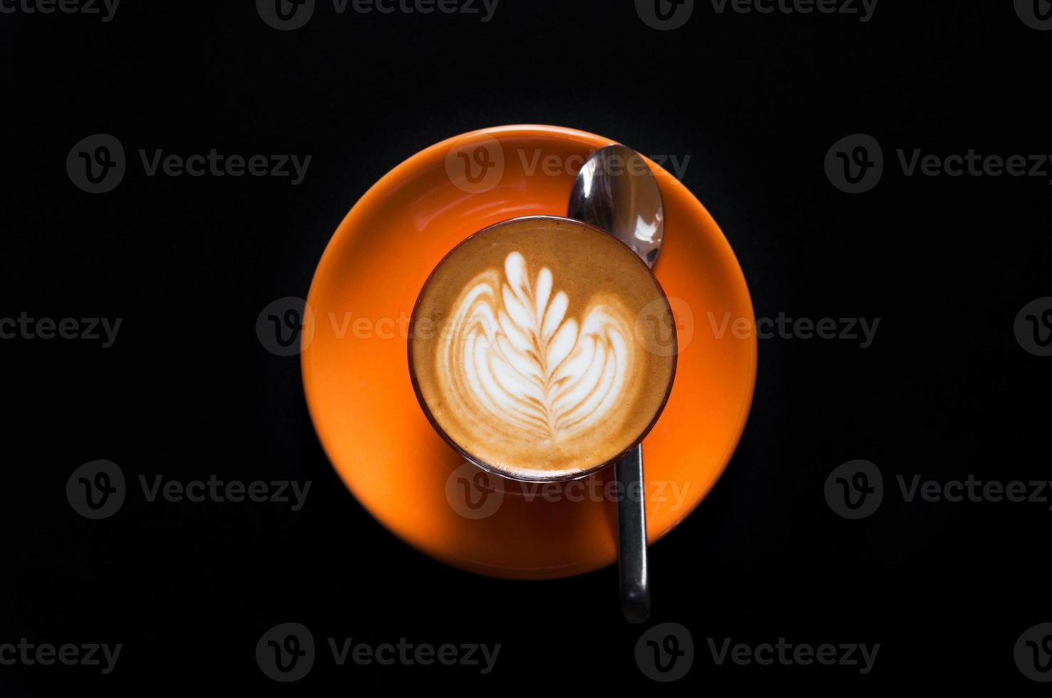 Hot latte in orange cup with floral pattern in foam on a dark background photo