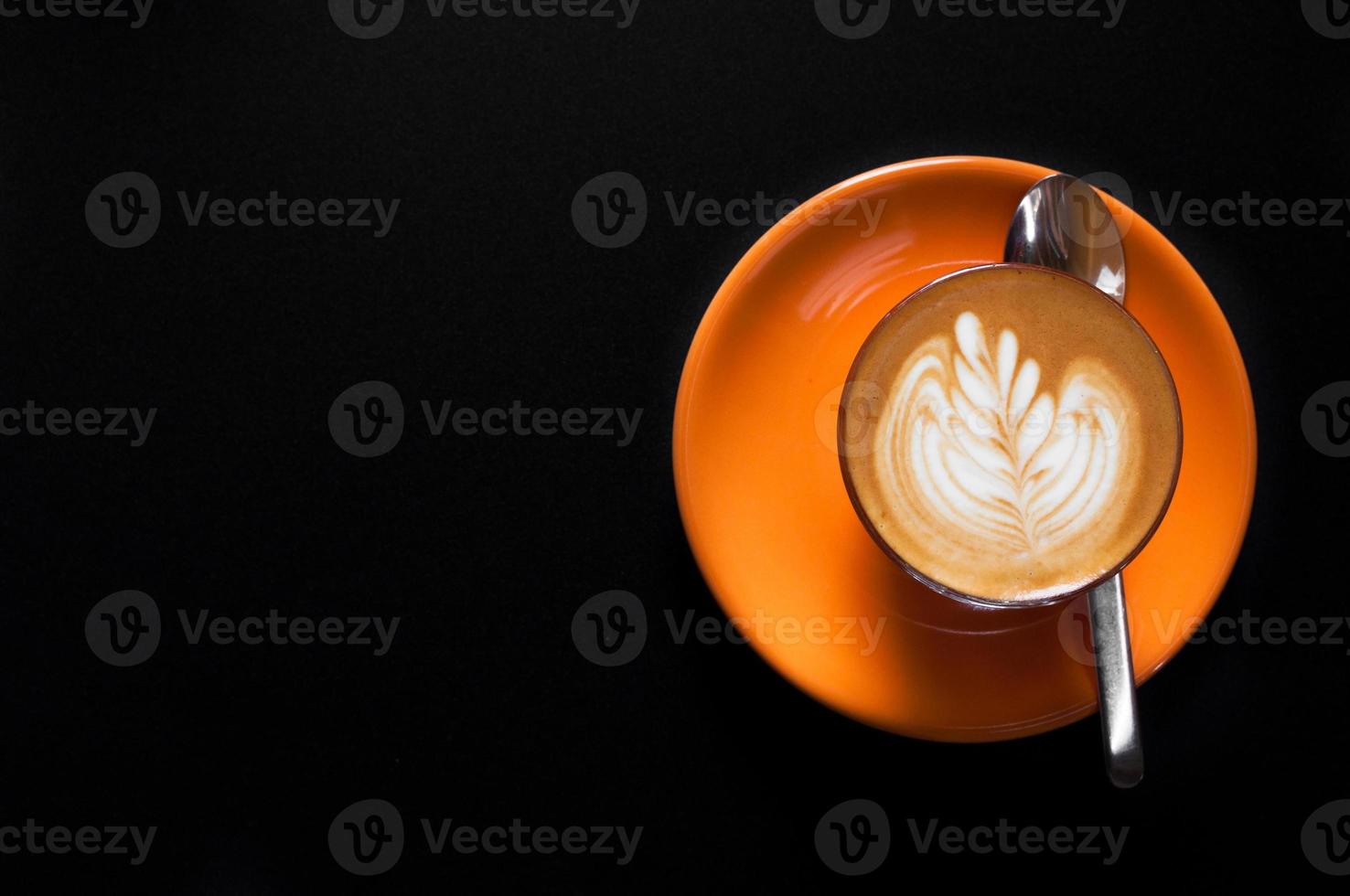 Hot latte in orange cup with floral pattern in foam on a dark background photo