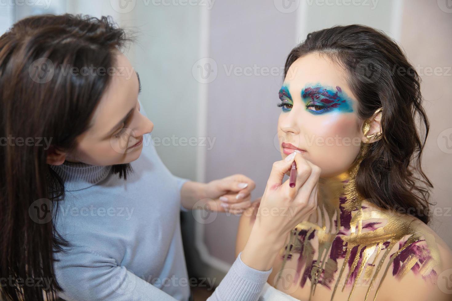 el artista aplica maquillaje a un encantador joven modelo foto