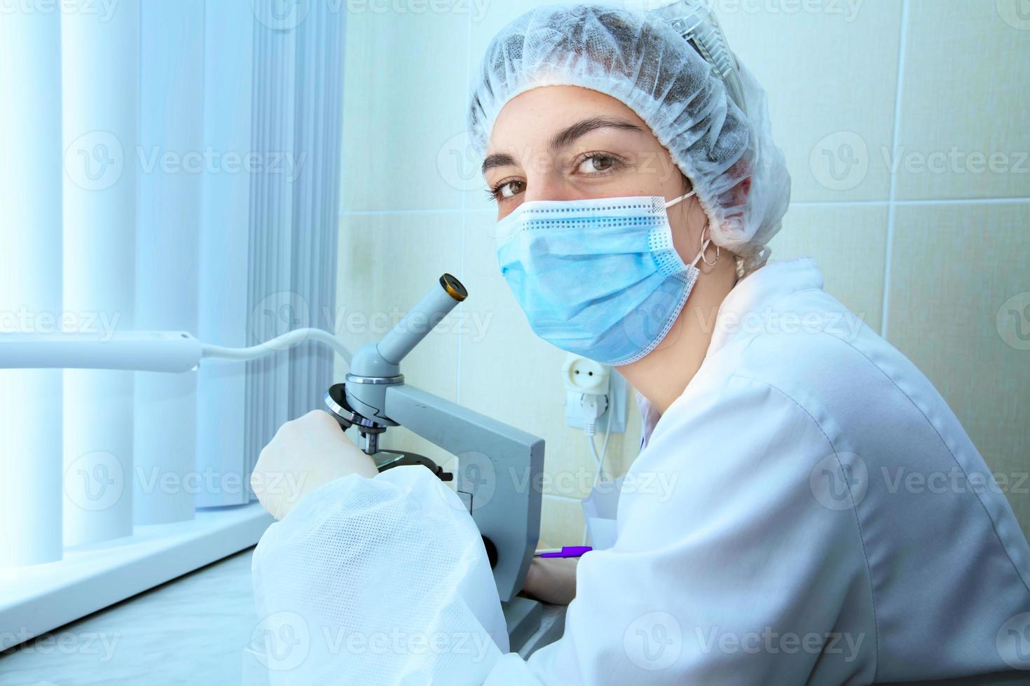 laboratorio asistente en un hospital con un microscopio. un profesional mujer científico es trabajando en un vacuna en un investigación laboratorio. lugar de trabajo de un genético ingeniero. tecnología y Ciencias concepto. foto