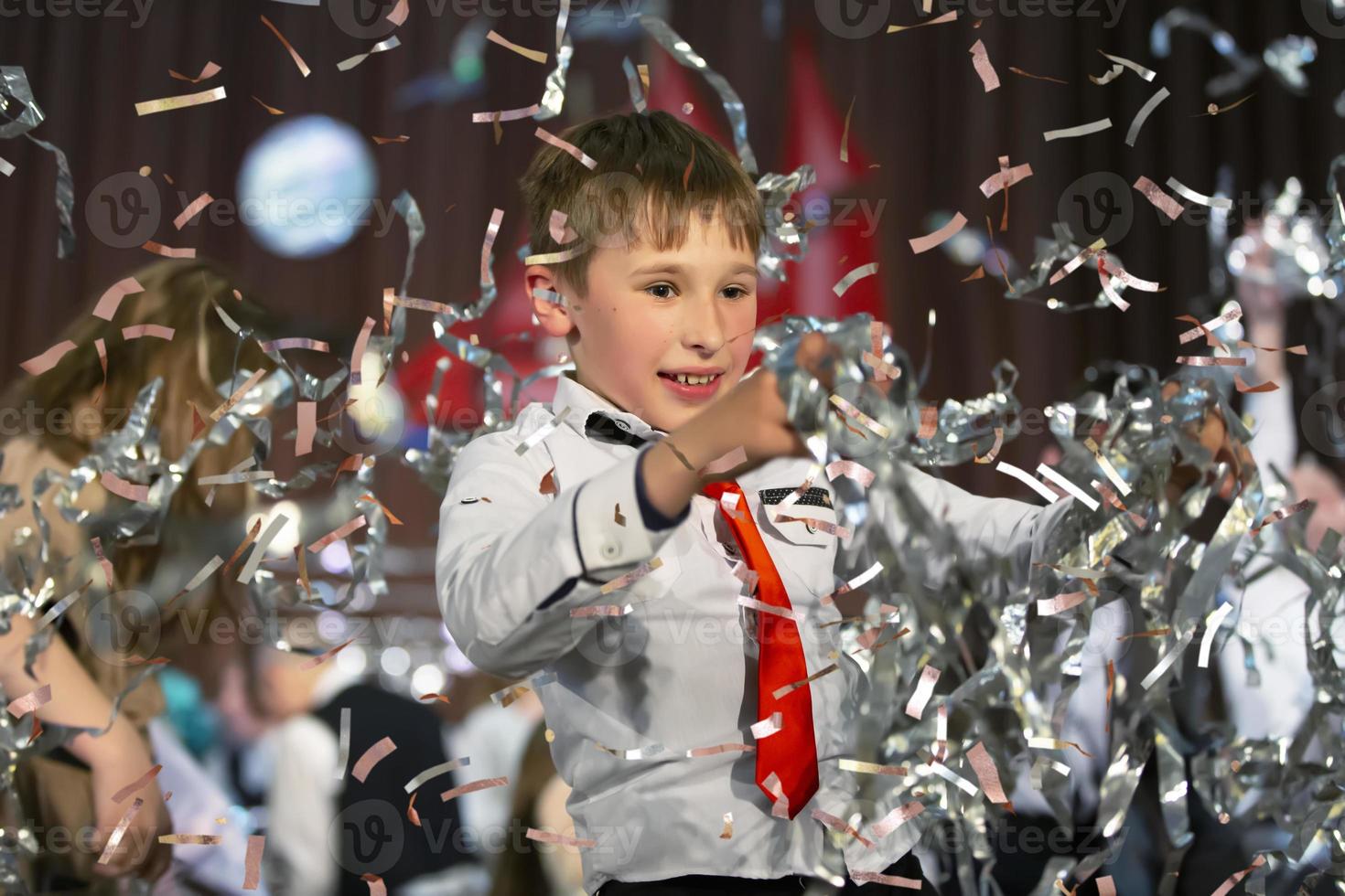 Happy little boy in confetti.Magic time - Portrait of a very happy child with hands smiling while falling confetti. At a children's party or birthday. photo