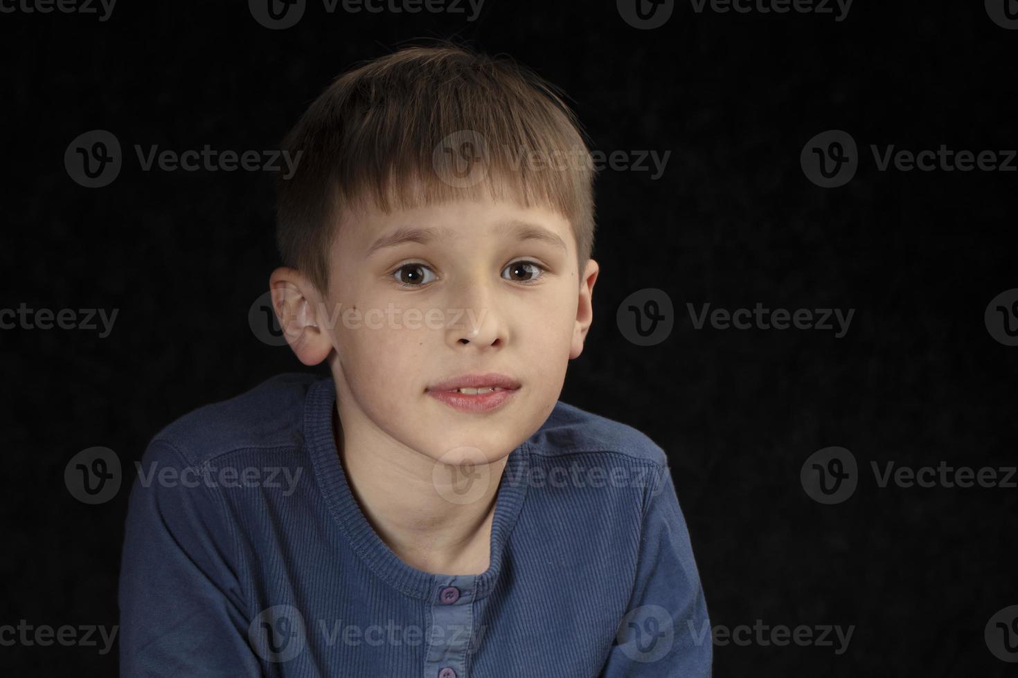 Portrait of a ten-year-old boy on a dark background. The child looks into the camera with intelligent eyes. Handsome boy of school age. photo