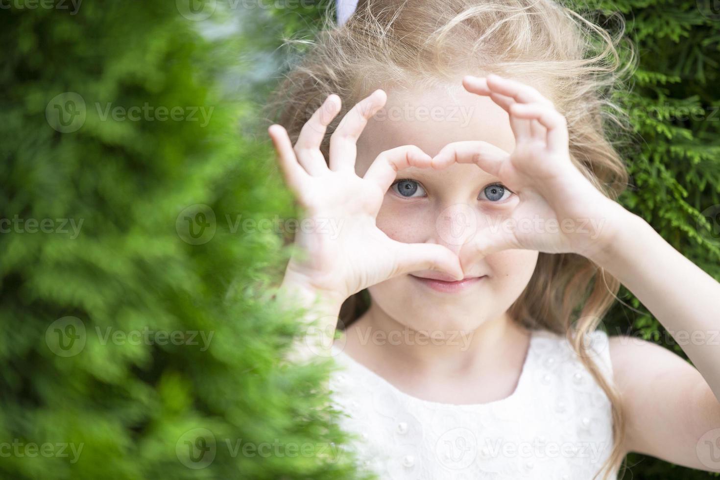 A little girl shows a heart sign with her fingers. photo