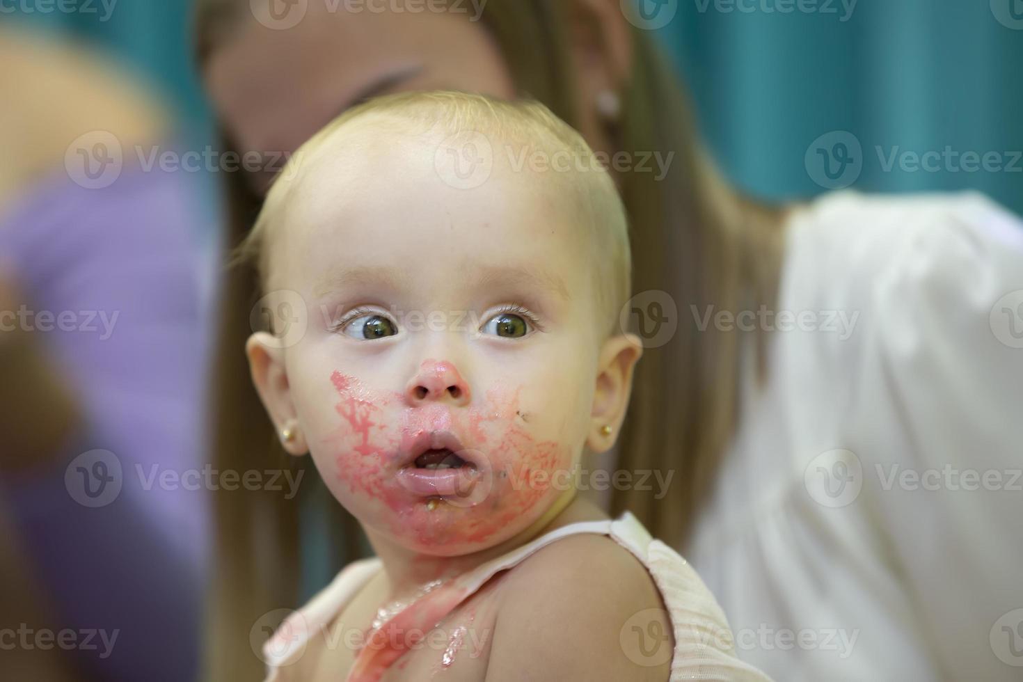 The little girl smeared her face with pink sweet cream. photo