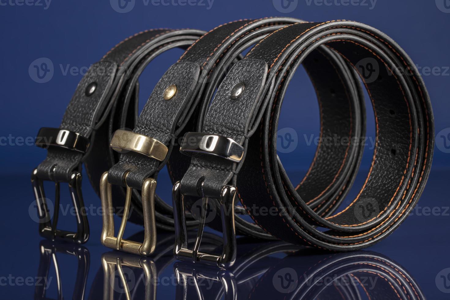 Group of black leather belts on a blue background. photo