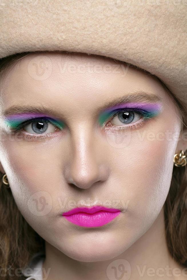 verticalmente el cara de un niña en un boina con brillante rosado constituir. de cerca de el cara de un de ojos azules belleza con brillante sombras de ojo sombra y lápiz labial. foto