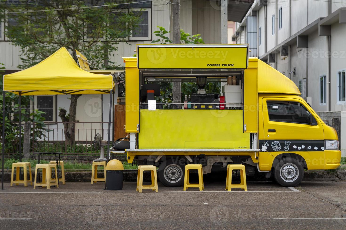 A small yellow truck converted into a mobile coffee shop with yellow seats and tents serving customers. photo