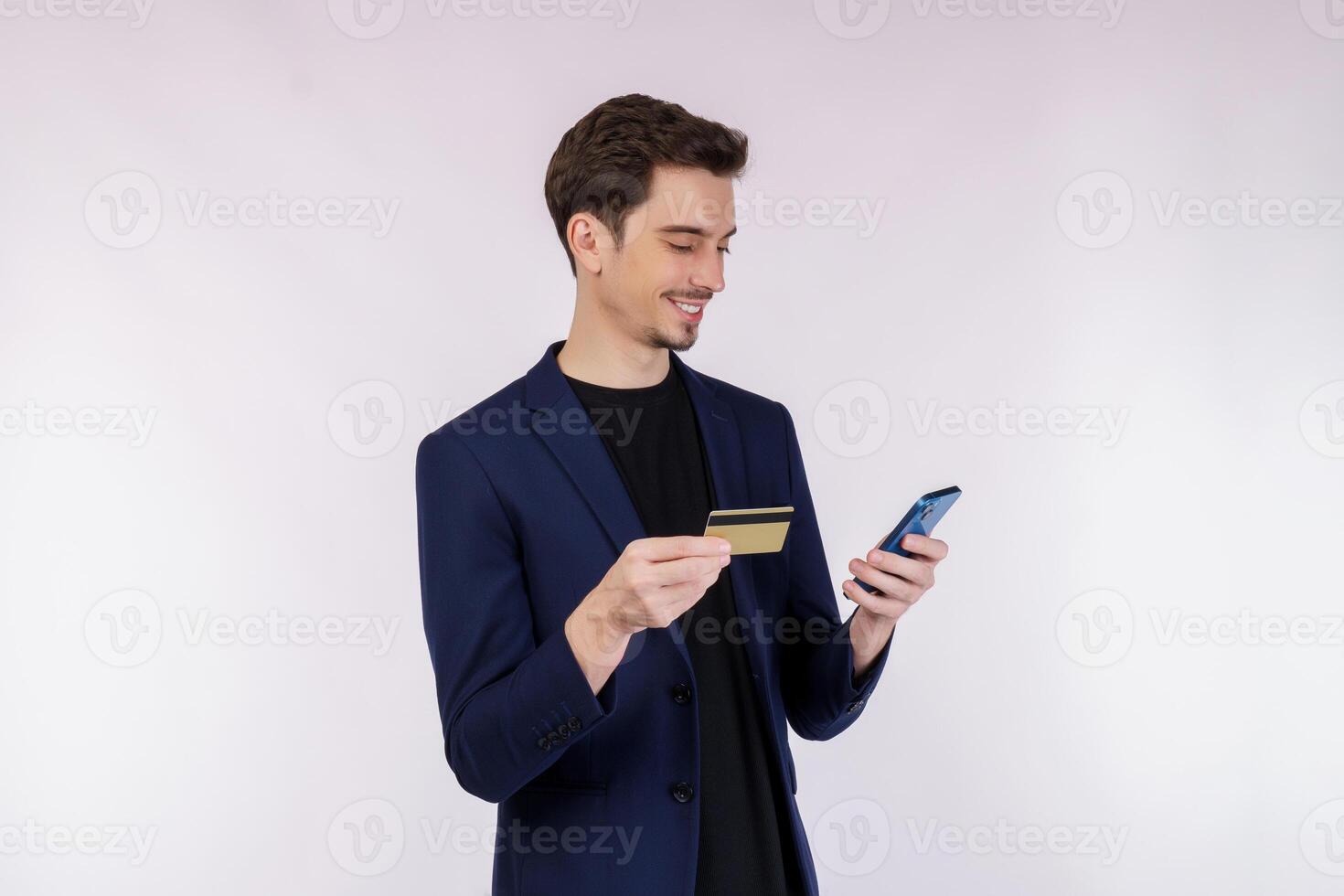 Portrait of happy young businessman standing using mobile cell phone and holding credit bank card isolated on white color background studio photo