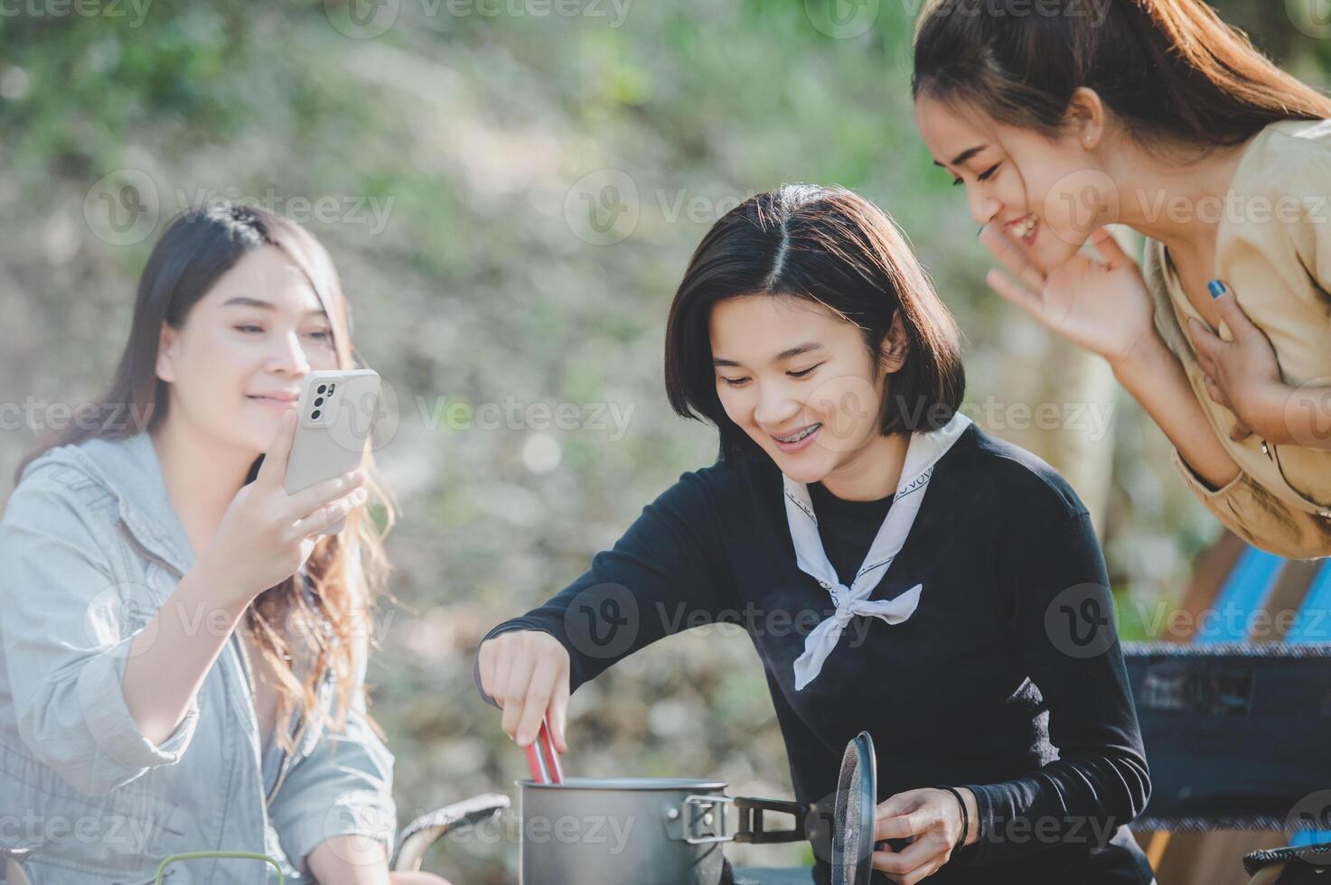 las mujeres jóvenes cocinan y usan el teléfono inteligente toman fotos en el campamento