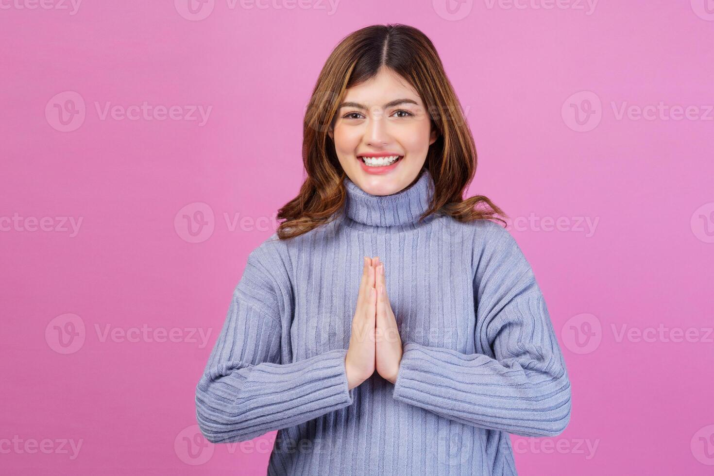 Portrait young happy cheerful woman paying respect, sawasdee symbol from Thailand greeting culture for hello or goodbye and looking at camera isolated pink background. photo