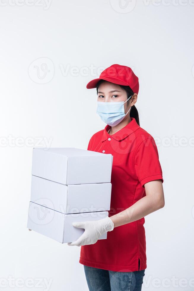 Image of a conscious young delivery man in red cap blank t-shirt uniform face mask gloves standing with empty white cardboard box isolated on light gray background studio photo