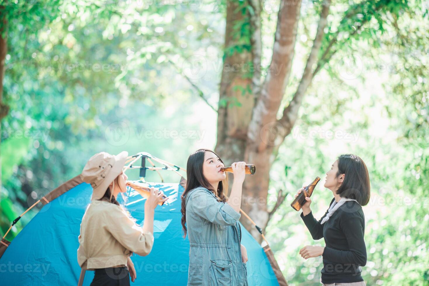 Young women cheer and drink beverage  front of camping tent photo