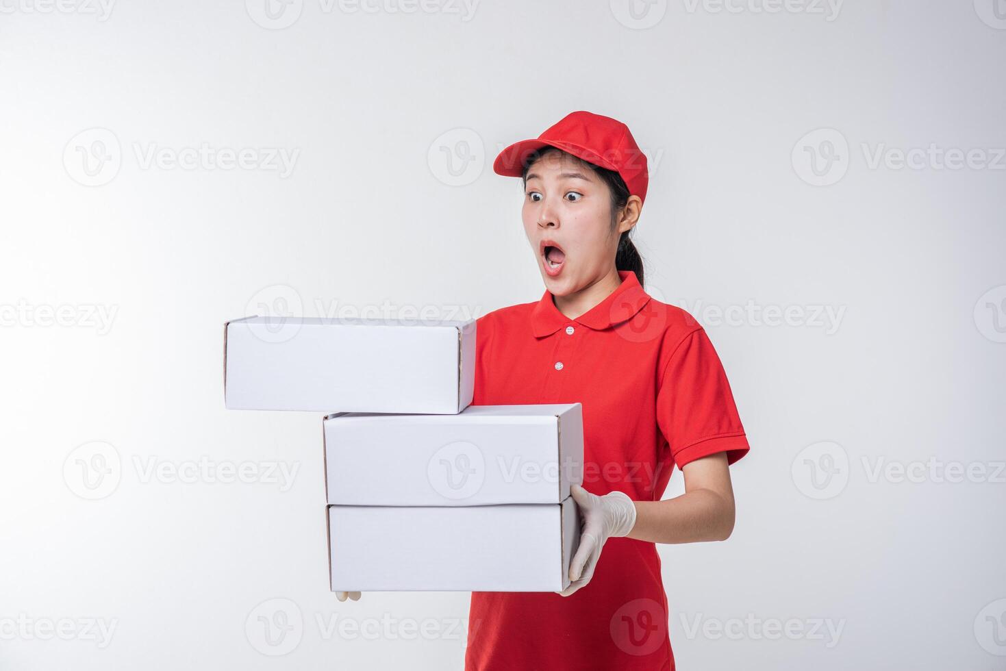 Image of  young delivery man in red cap blank t-shirt uniform standing with empty white cardboard box isolated on light gray background studio photo