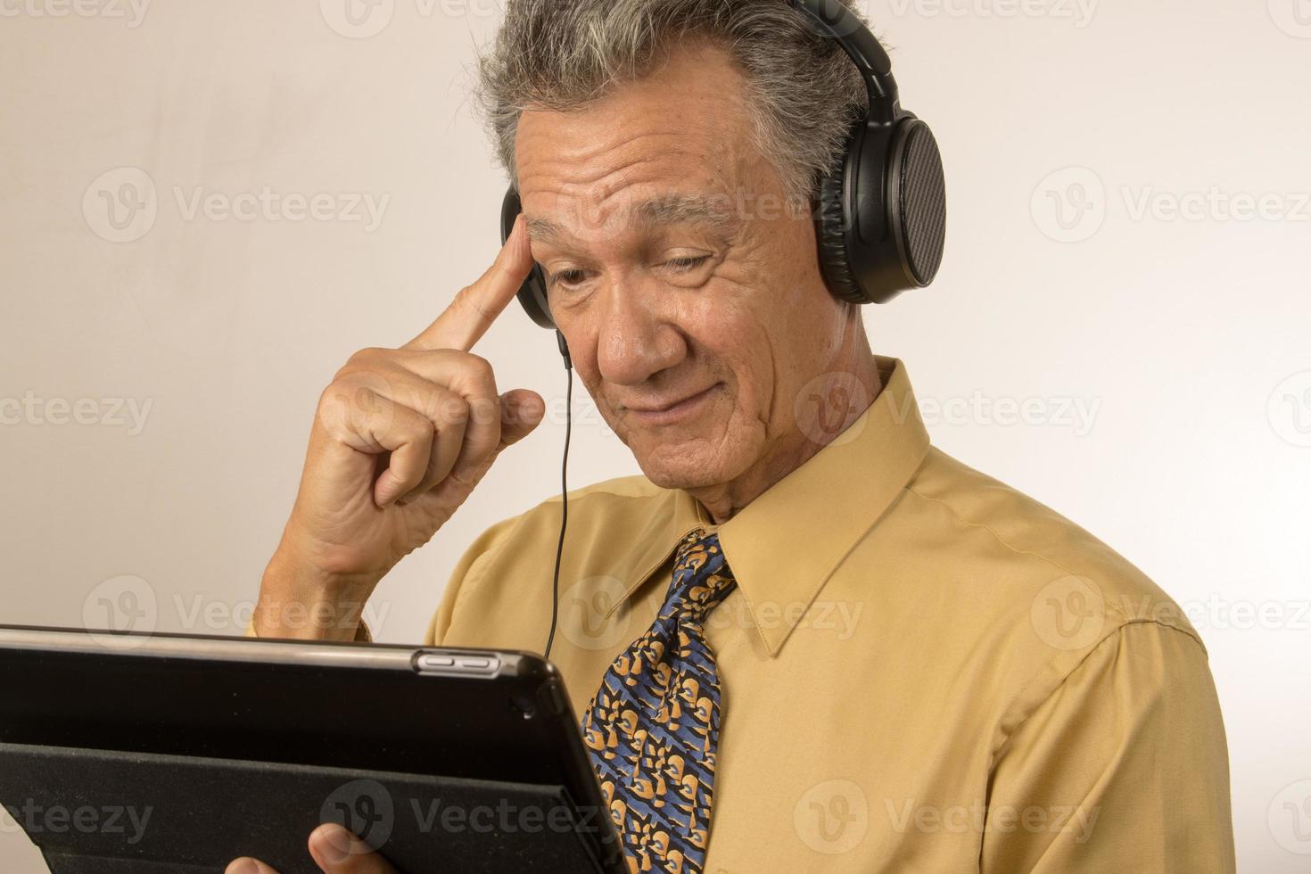 Older Man listening to music or a podcast wearing head phone on his smart tablet photo