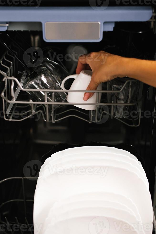 Woman loads dishes into the built-in dishwasher cups, glasses, plates. Type of hand and dishes photo