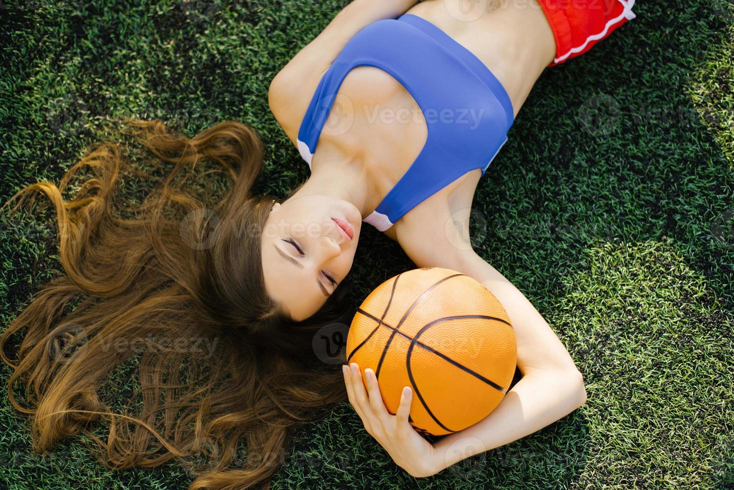 Attractive athletic young woman posing outdoors, lying on her back on the lawn and holding a basketball photo