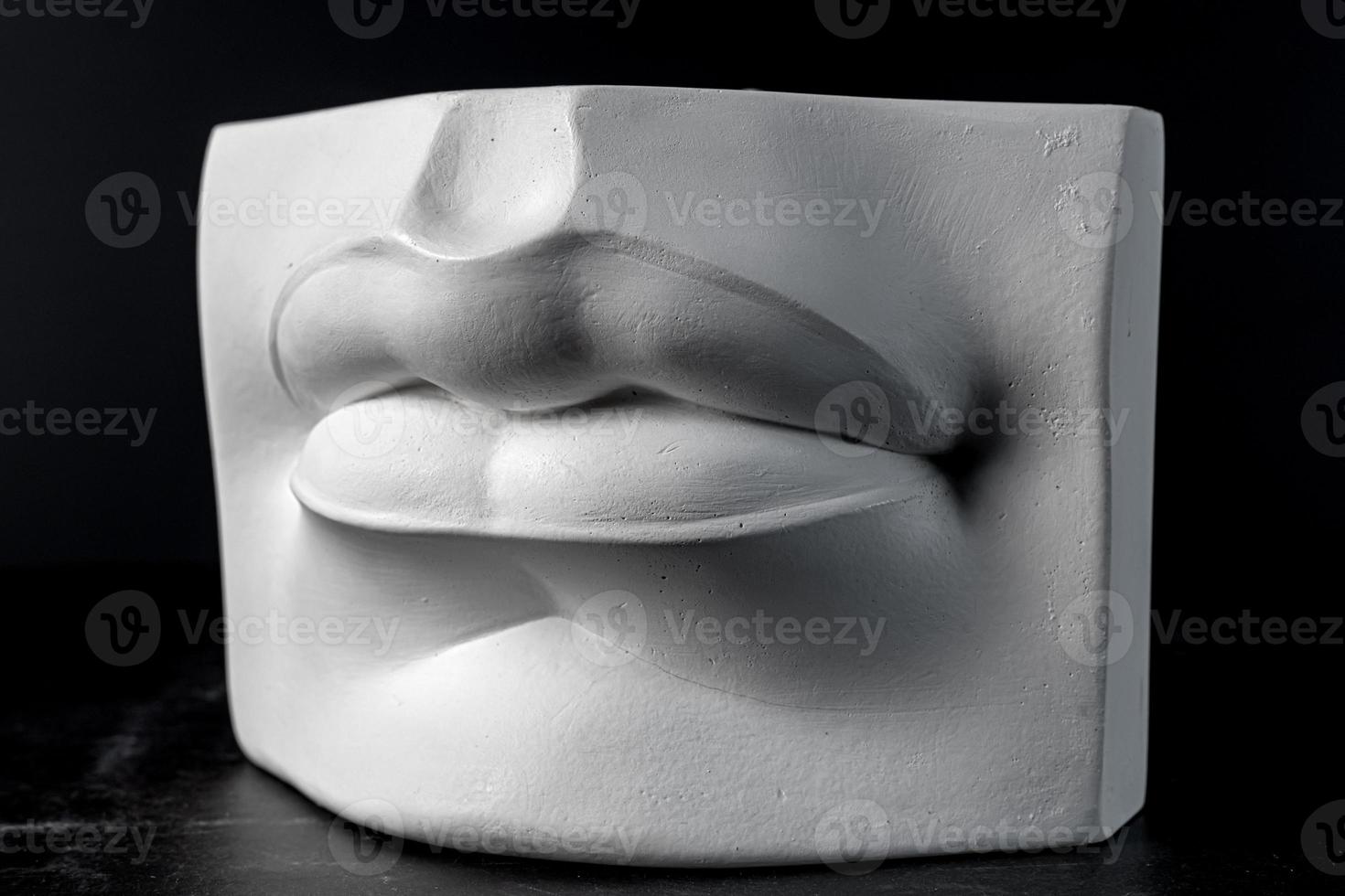 Plaster lips. A fragment of a plaster sculpture of a human face on a black background. photo