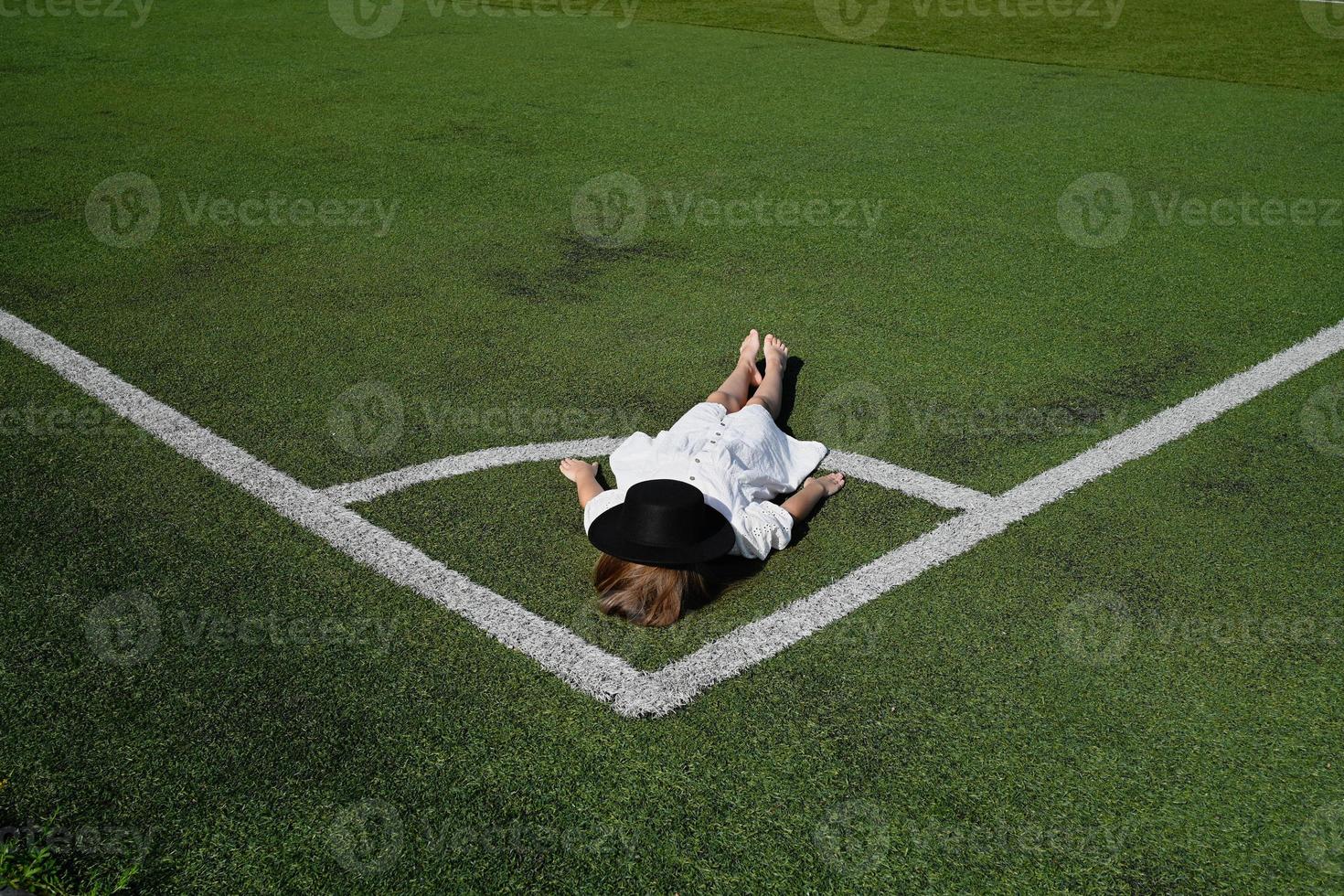 A girl in a hat, lying in the stadium. Active recreation in a white dress photo
