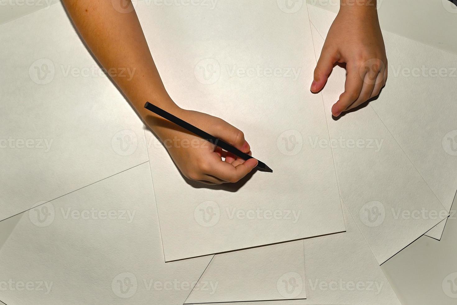 Close-up of children's hands drawing with a pencil on white paper. In the process of work. photo