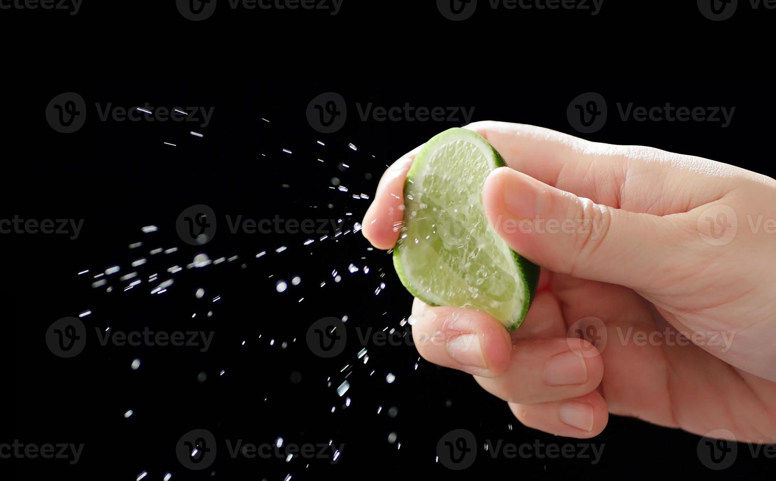 Close up of hand squeezing lemon, black background, splash of water photo