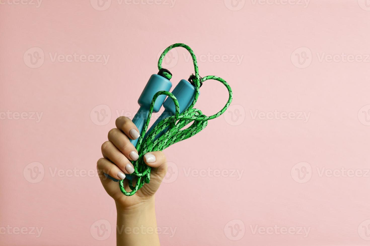 Womans hand with blue skipping rope on pink background photo