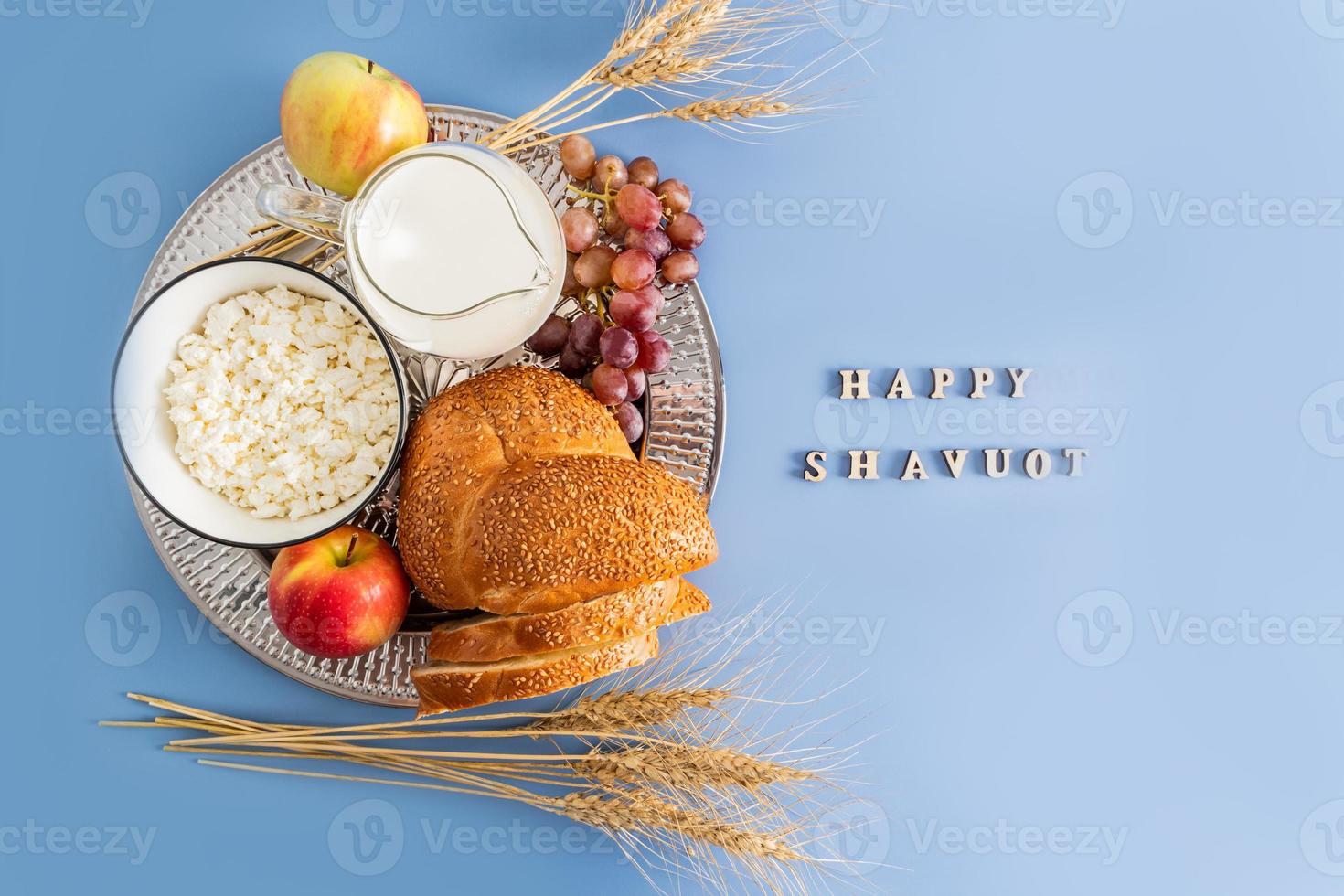 a silver dish with traditional treats for the spring holiday of Shavuot. top view. blue background with the letters -happy shavuot. photo