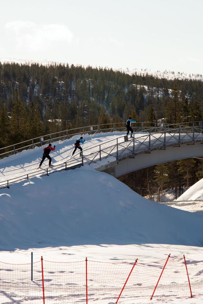 Three people crossing a bridge doing cross country ski photo