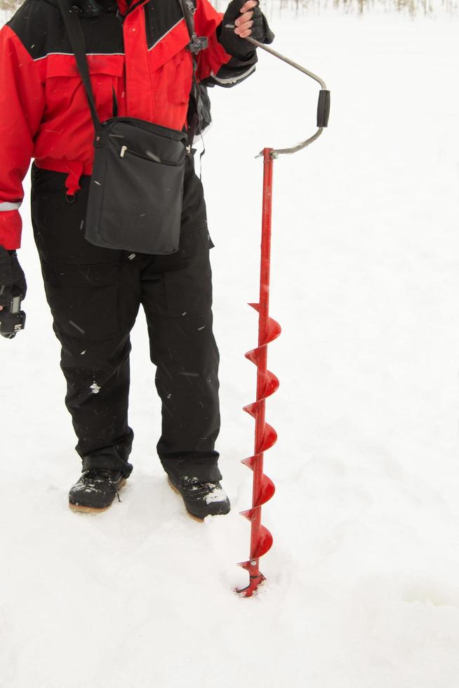 irreconocible persona haciendo un agujero en un con hielo lago para pescar foto