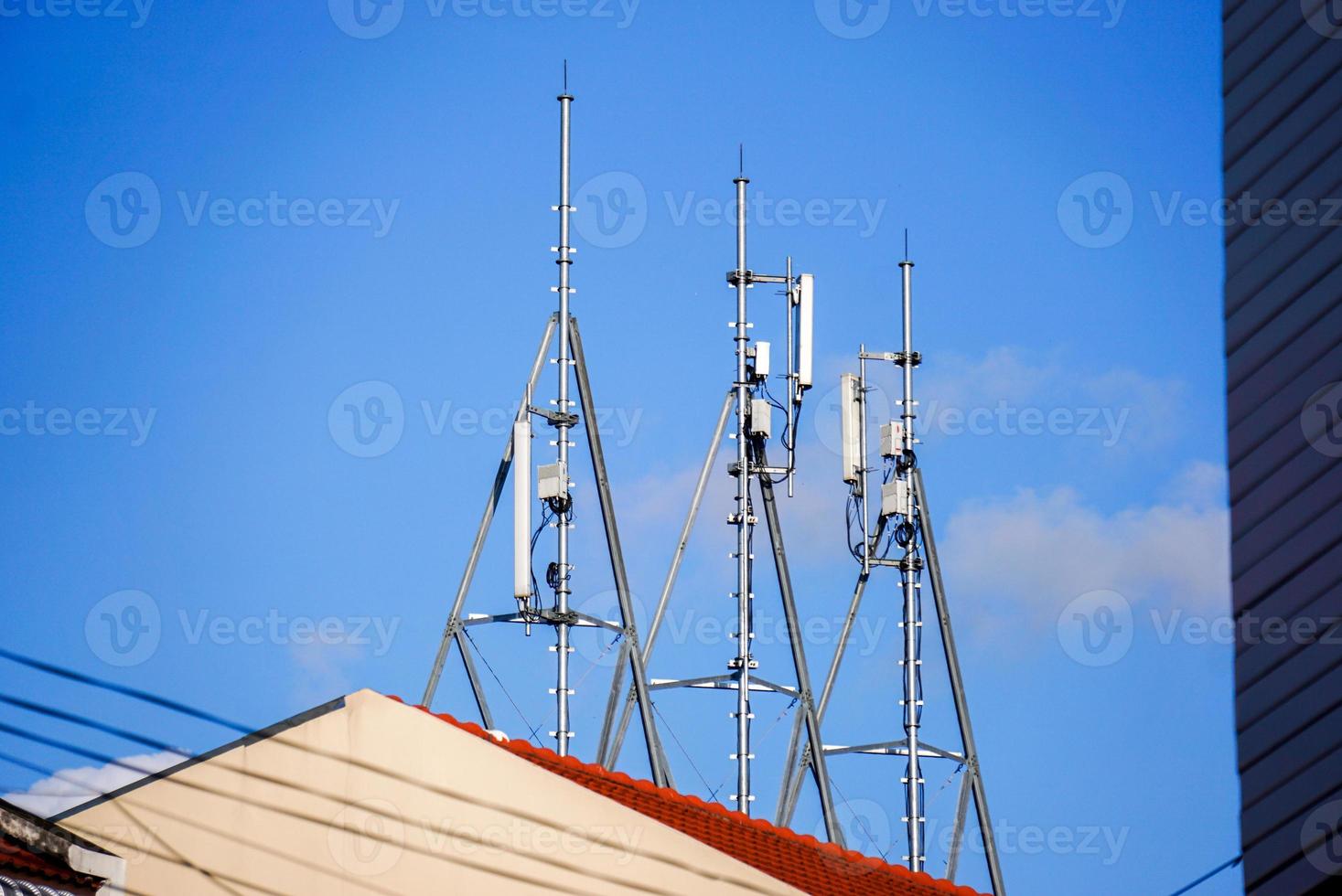 Look up view of communication tower with antennas on the top of building and bright blue sky background. photo