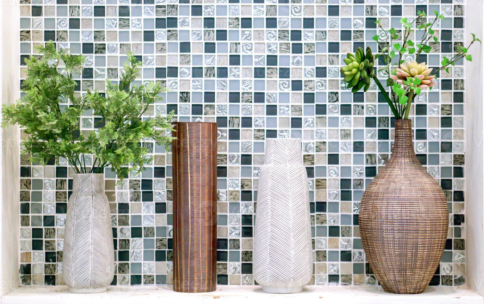 Ornamental plants in different vases put on white shelf front of square pattern tile in the toilet. photo