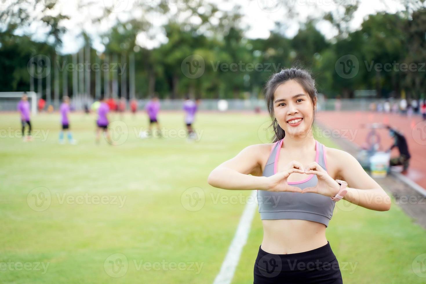 joven hembra vestir un ropa deportiva haciendo un corazón conformado manos a el fútbol americano estadio en el Mañana. ella tener un hermosa sonrisa foto