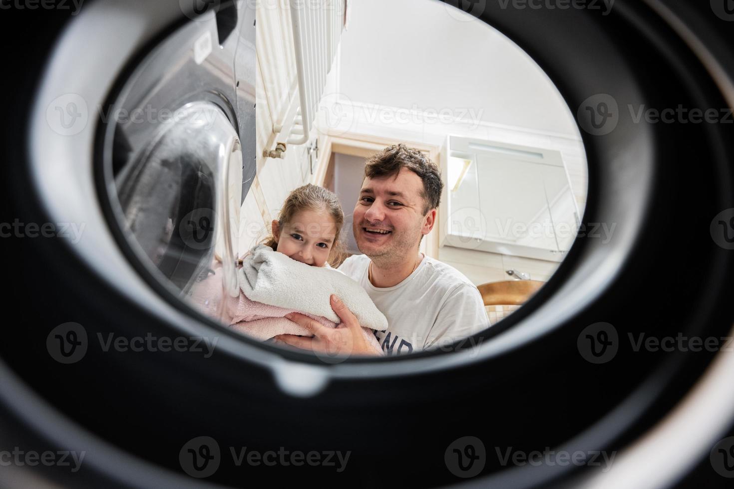 Man and girl view from washing machine inside. Father with daughter does laundry daily routine. photo