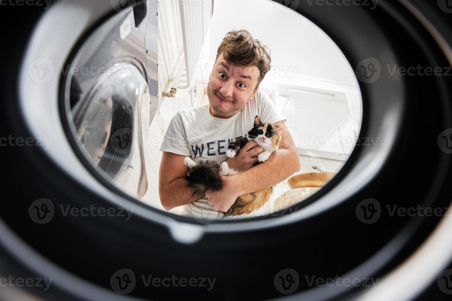 hombre con gato ver desde Lavado máquina adentro. masculino lo hace lavandería diario rutina. foto