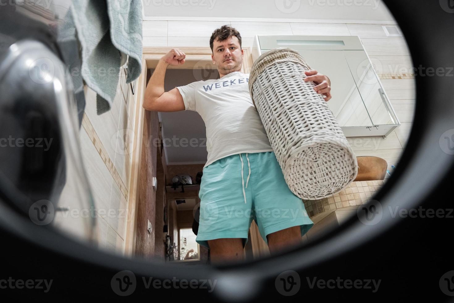 Man with basket, view from washing machine inside. Male does laundry daily routine. Show his muscle. photo
