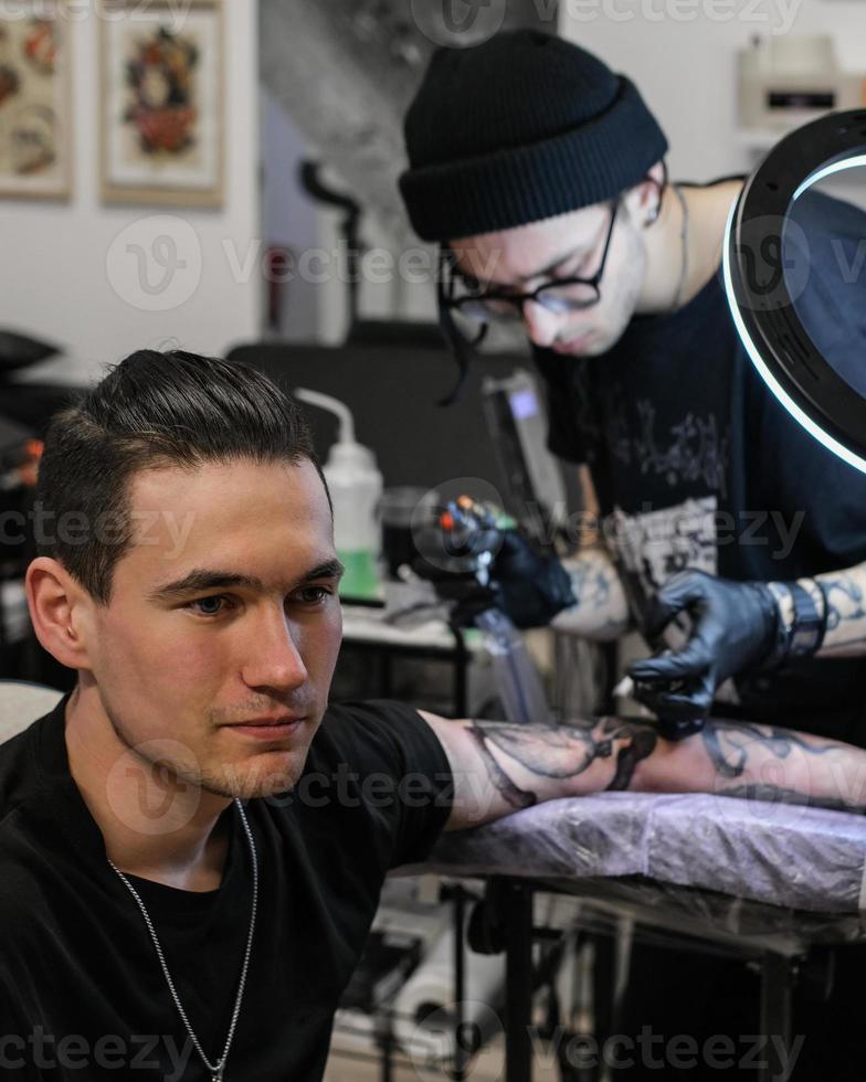 Professional tattoo artist stuffs a tattoo on the man's hand. Tattoo artist at work. Tattoo creation process. Art and creativity photo