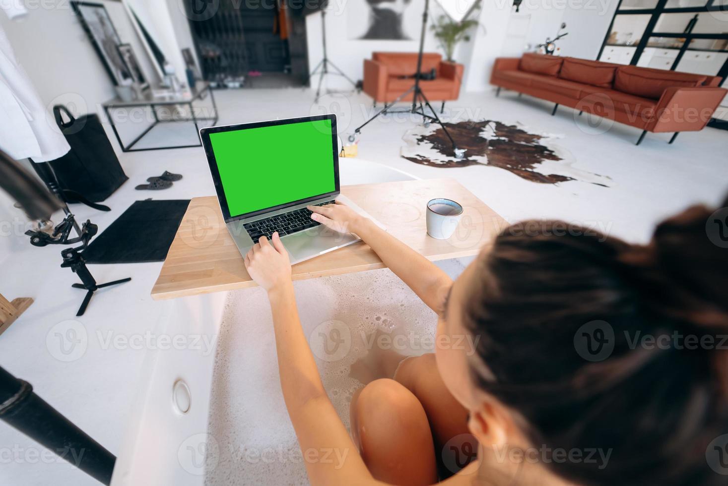 Young woman working on laptop while taking a bathtub photo