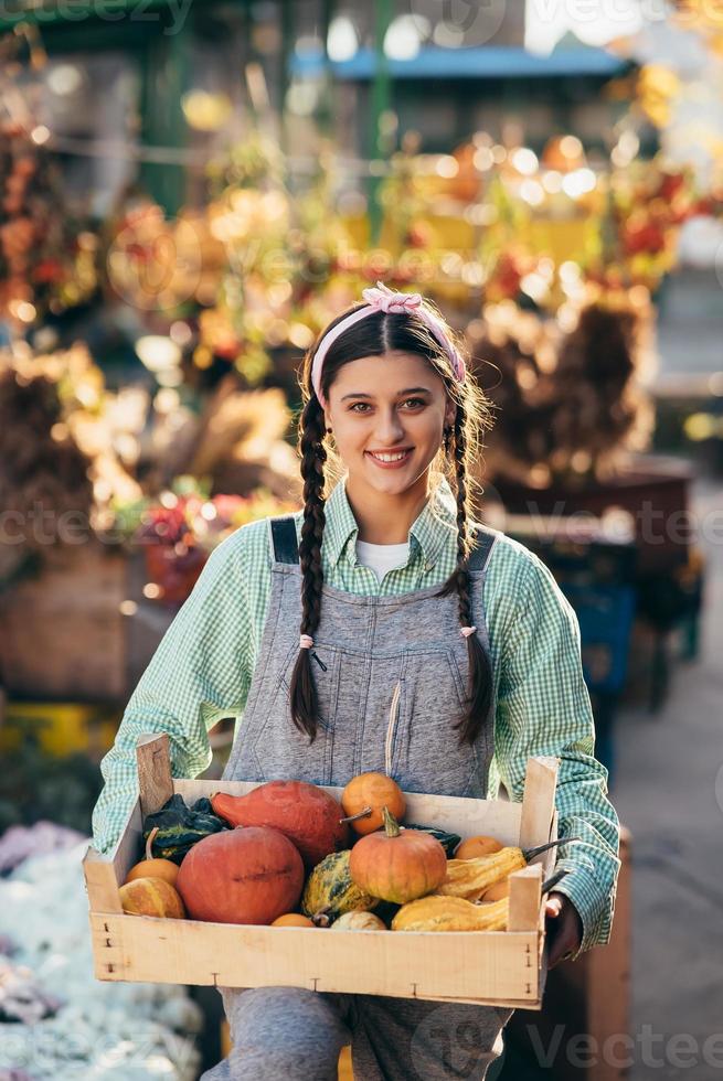 Farmer woman holds a wooden box with pumpkins in hands photo