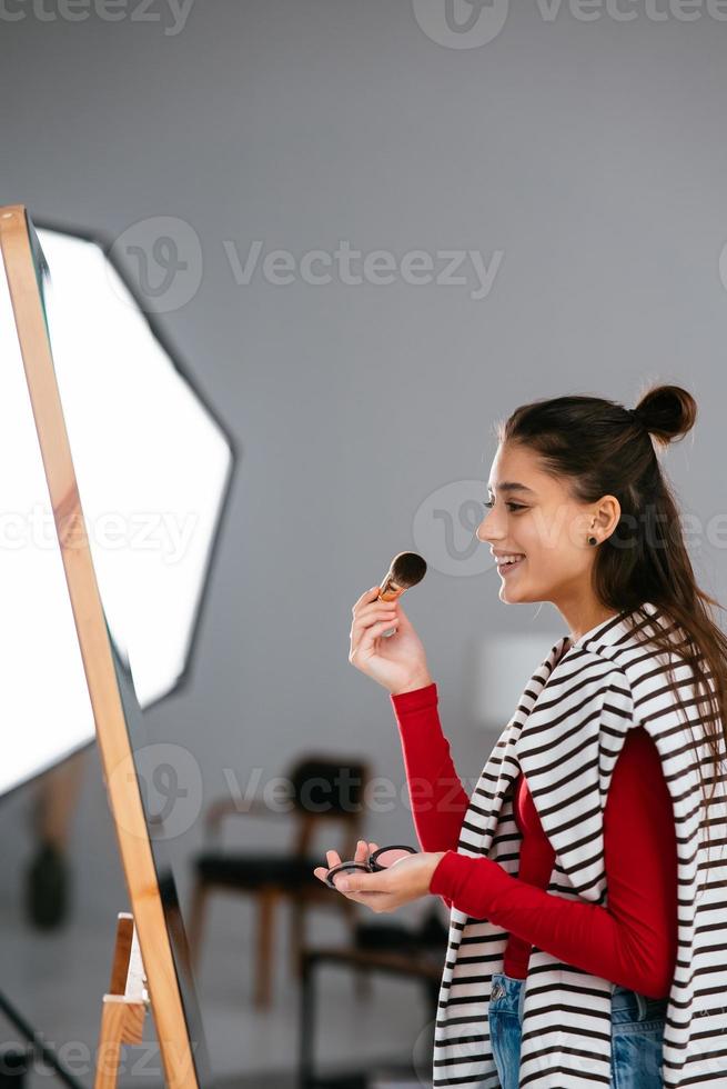 Young woman applies makeup on her face in front of the mirror photo