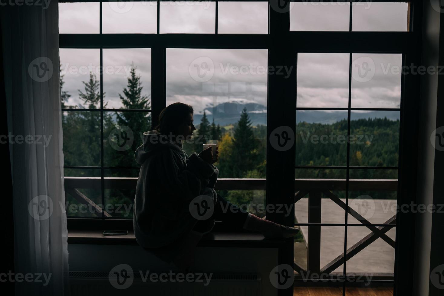 silueta de una mujer sentada en el alféizar de la ventana con una taza foto