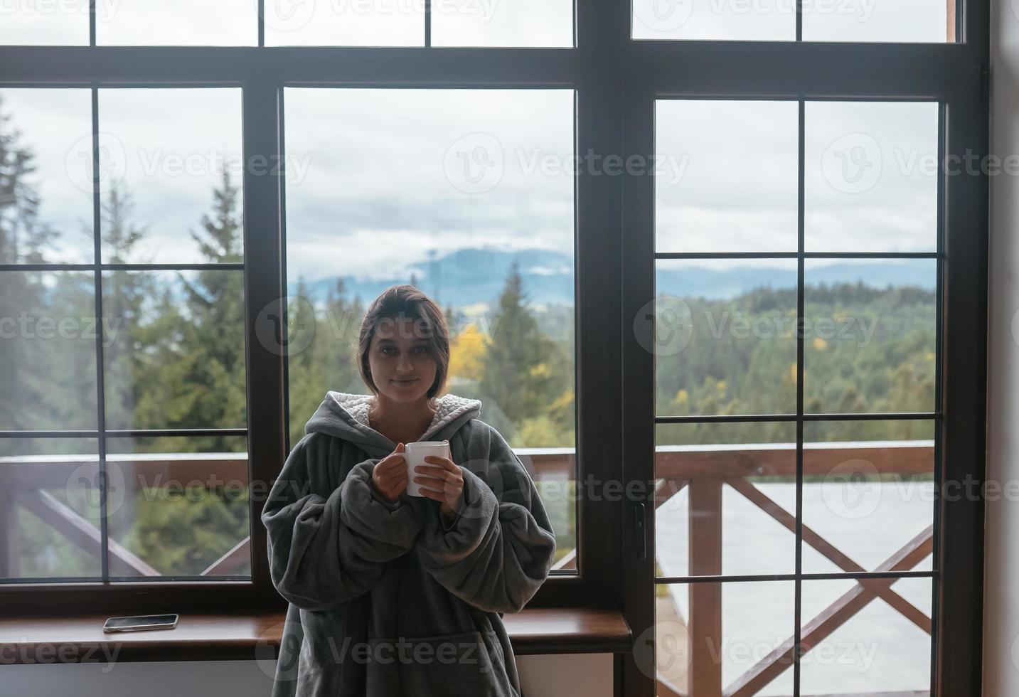 Young woman standing by the window holds a mug photo