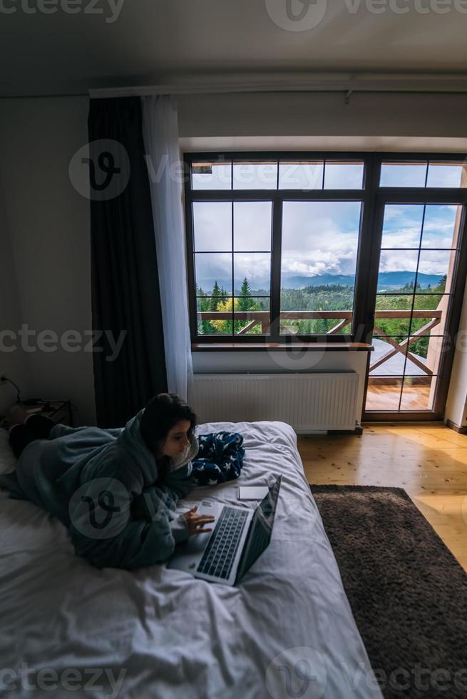 Young woman working on laptop while lying on bed photo
