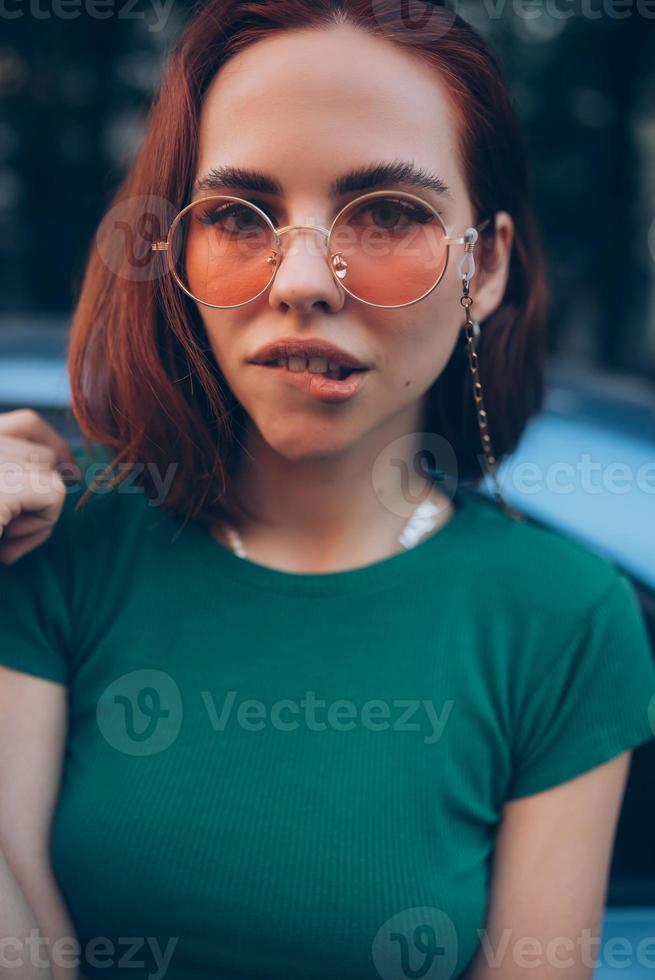Beautiful fashionable young woman in glasses posing near car photo